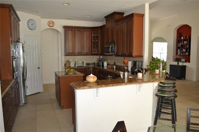 kitchen with light tile patterned floors, a kitchen island, appliances with stainless steel finishes, a peninsula, and a kitchen bar