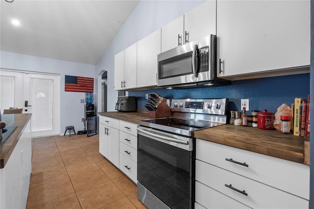 kitchen featuring arched walkways, light tile patterned floors, wooden counters, appliances with stainless steel finishes, and white cabinetry