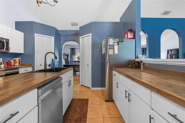 kitchen featuring light tile patterned floors, appliances with stainless steel finishes, white cabinetry, wooden counters, and a sink