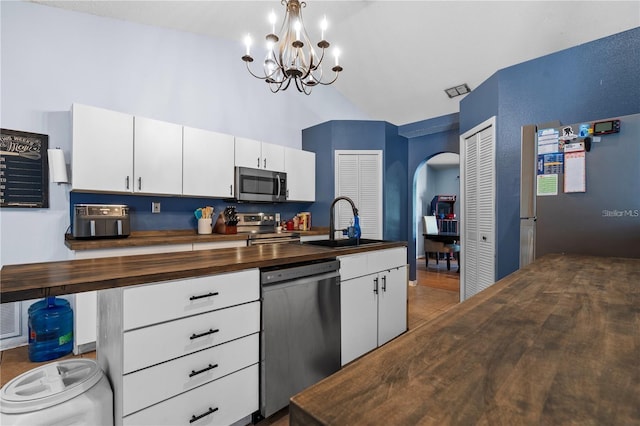 kitchen with arched walkways, stainless steel appliances, lofted ceiling, a sink, and butcher block countertops