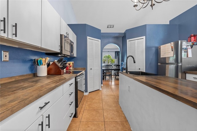 kitchen featuring arched walkways, light tile patterned floors, stainless steel appliances, butcher block countertops, and a sink