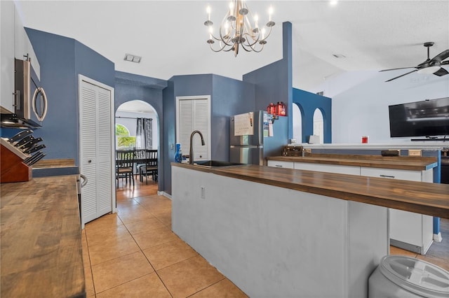 kitchen featuring arched walkways, stainless steel appliances, butcher block counters, light tile patterned flooring, and ceiling fan with notable chandelier