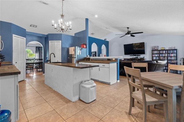 kitchen featuring freestanding refrigerator, light tile patterned flooring, a center island with sink, and arched walkways