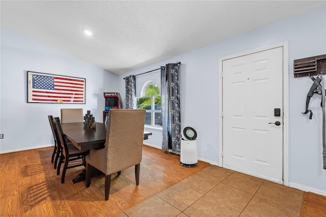 dining space with lofted ceiling, light wood finished floors, a textured ceiling, and baseboards