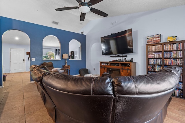 tiled living area with arched walkways, visible vents, vaulted ceiling, a textured ceiling, and ceiling fan