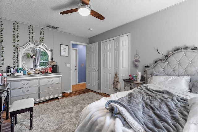 bedroom with a textured ceiling, ceiling fan, wood finished floors, visible vents, and a closet