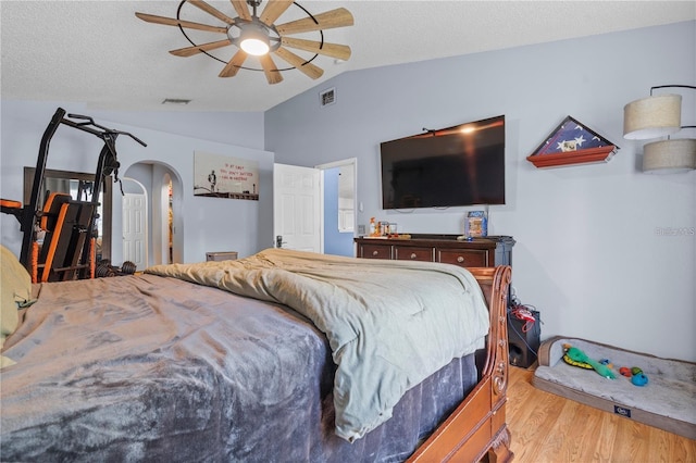 bedroom with visible vents, arched walkways, light wood-style flooring, vaulted ceiling, and a textured ceiling