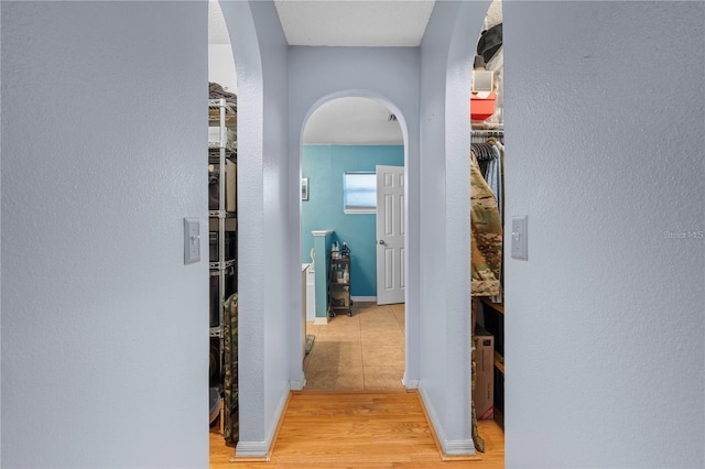 corridor featuring light wood-style floors, baseboards, and arched walkways