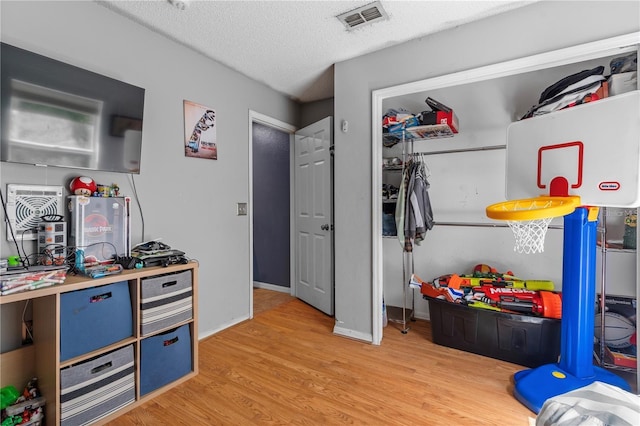 rec room with baseboards, light wood-style flooring, visible vents, and a textured ceiling