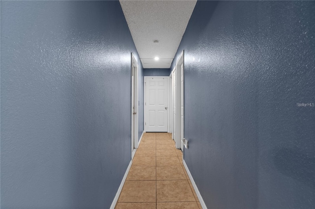 hallway featuring light tile patterned floors, baseboards, a textured ceiling, and a textured wall