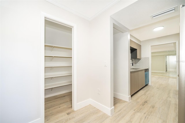 hall with light wood-type flooring, baseboards, visible vents, and a sink