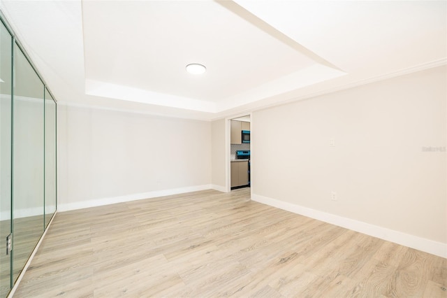 spare room featuring light wood finished floors, a raised ceiling, and baseboards