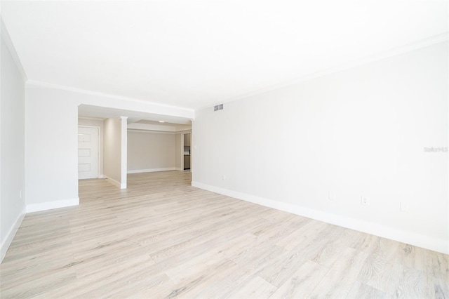 empty room with light wood finished floors, baseboards, visible vents, and crown molding