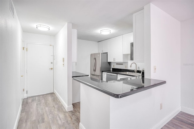 kitchen with light wood-style flooring, a sink, stainless steel appliances, white cabinetry, and dark countertops