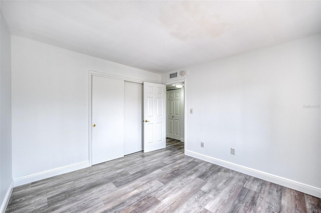 unfurnished bedroom with visible vents, wood finished floors, a closet, and baseboards