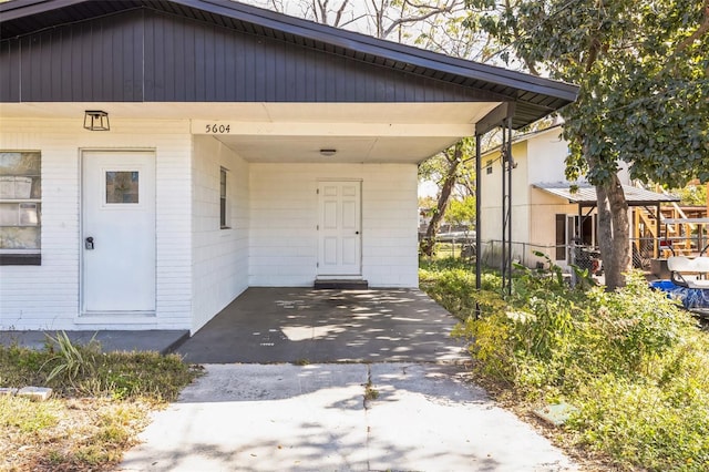 doorway to property with driveway, fence, and an attached carport