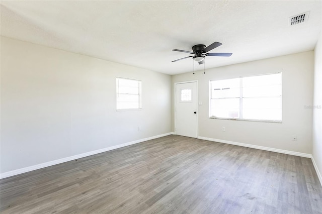 empty room with a ceiling fan, baseboards, visible vents, and wood finished floors