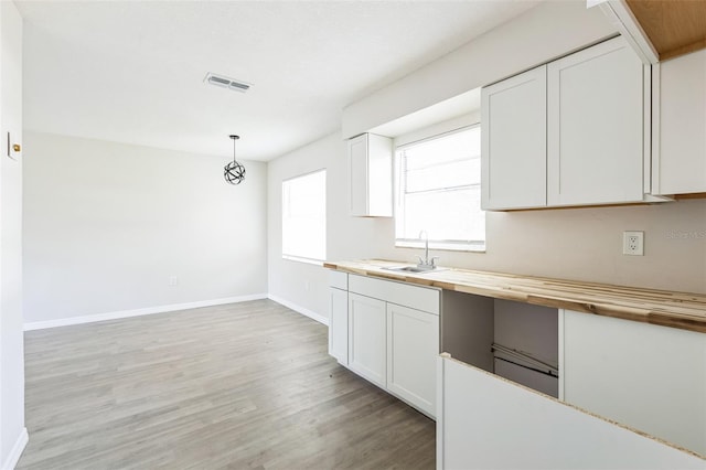 kitchen featuring light wood finished floors, visible vents, wooden counters, white cabinets, and a sink