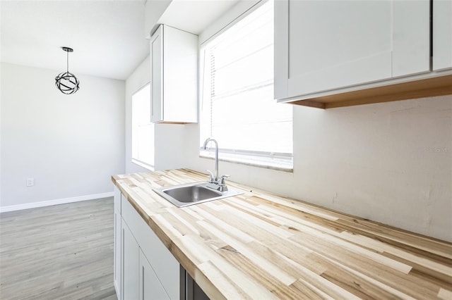 kitchen featuring light wood finished floors, hanging light fixtures, white cabinetry, a sink, and baseboards