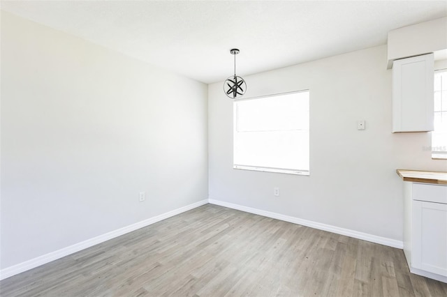 unfurnished dining area with plenty of natural light, light wood-style flooring, and baseboards