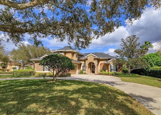 mediterranean / spanish home with an attached garage, stone siding, a front lawn, and concrete driveway