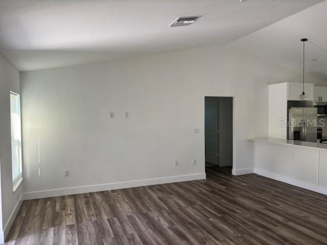 unfurnished living room with lofted ceiling, baseboards, visible vents, and dark wood-type flooring