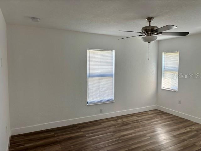 spare room featuring dark wood-style flooring, ceiling fan, and baseboards