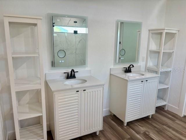 full bath with two vanities, a sink, a marble finish shower, and wood finished floors