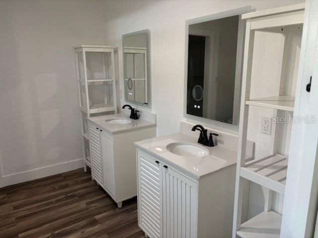 bathroom featuring two vanities, a sink, baseboards, and wood finished floors