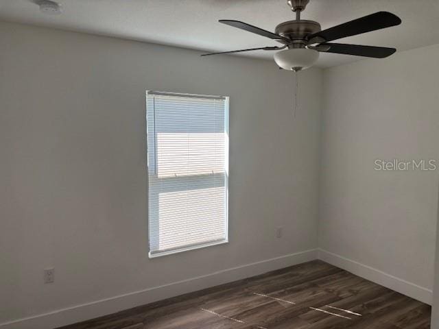 empty room with ceiling fan, dark wood finished floors, and baseboards