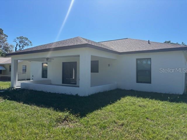 rear view of property featuring a lawn and stucco siding