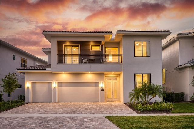 view of front facade featuring a tiled roof, decorative driveway, a balcony, and stucco siding