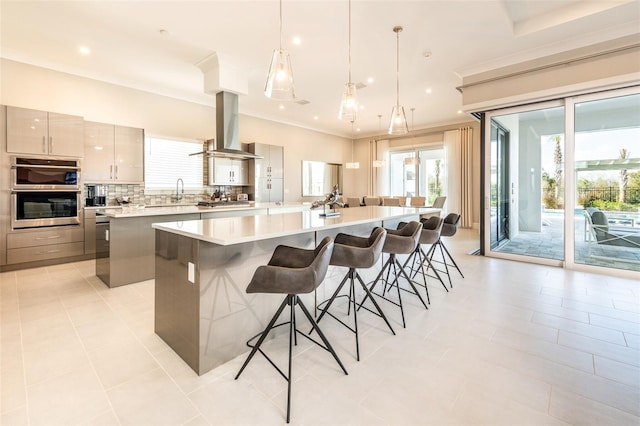 kitchen featuring light countertops, a large island, decorative backsplash, modern cabinets, and island exhaust hood