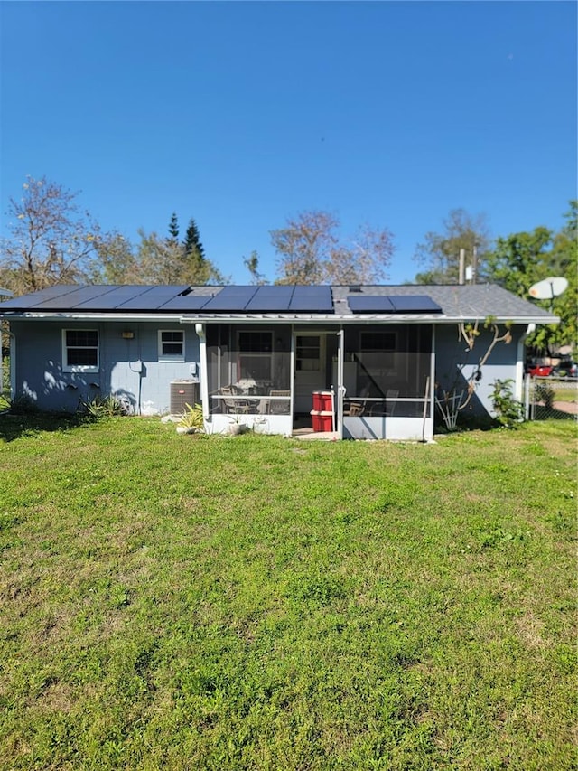 rear view of property featuring a lawn, a sunroom, and roof mounted solar panels