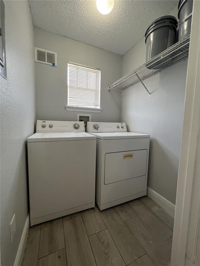 clothes washing area with a textured ceiling, laundry area, visible vents, washer and dryer, and light wood-type flooring