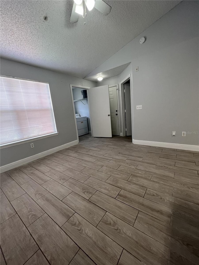 empty room featuring lofted ceiling, a textured ceiling, a ceiling fan, baseboards, and wood tiled floor