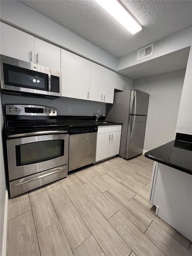 kitchen featuring visible vents, appliances with stainless steel finishes, white cabinets, and wood finish floors