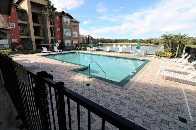 community pool with a water view, fence, and a patio