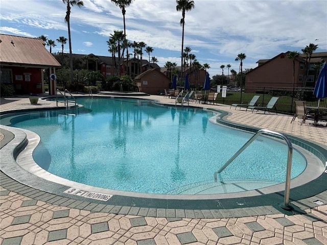 pool with a patio area, fence, and a jacuzzi