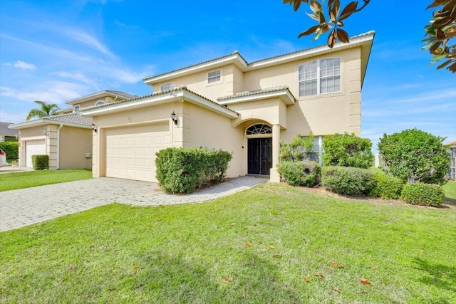 mediterranean / spanish house featuring an attached garage, a tiled roof, decorative driveway, stucco siding, and a front lawn