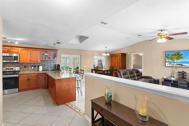 kitchen featuring light tile patterned floors, decorative backsplash, appliances with stainless steel finishes, brown cabinets, and a peninsula