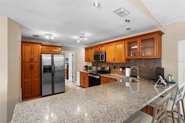 kitchen with a sink, visible vents, appliances with stainless steel finishes, tasteful backsplash, and brown cabinetry