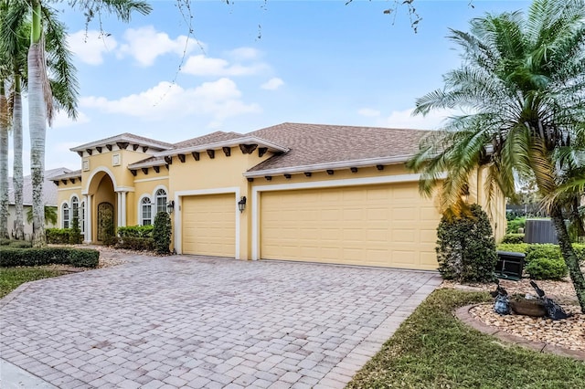 mediterranean / spanish-style house with decorative driveway, central AC unit, an attached garage, and stucco siding