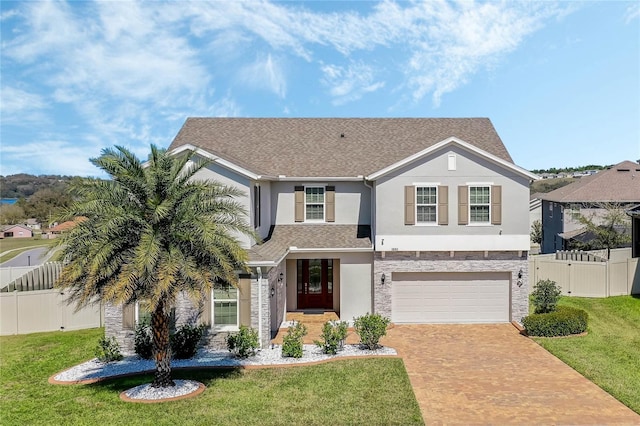 traditional home featuring an attached garage, fence, decorative driveway, stucco siding, and a front yard