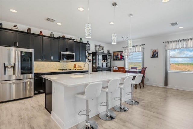 kitchen with tasteful backsplash, an island with sink, stainless steel appliances, light countertops, and a sink