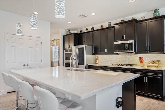 kitchen featuring a kitchen island with sink, stainless steel appliances, visible vents, a kitchen breakfast bar, and decorative backsplash