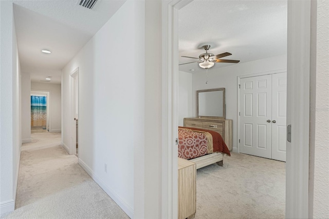 hallway with baseboards, visible vents, a textured ceiling, and light colored carpet