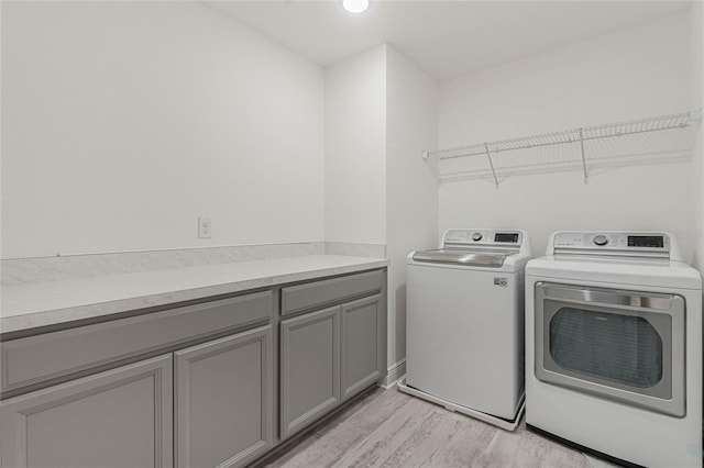 clothes washing area with washing machine and dryer and light wood-style flooring