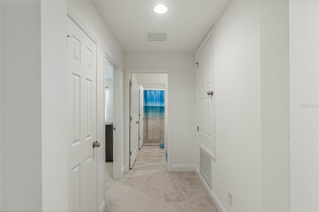 hall with light colored carpet, visible vents, and baseboards