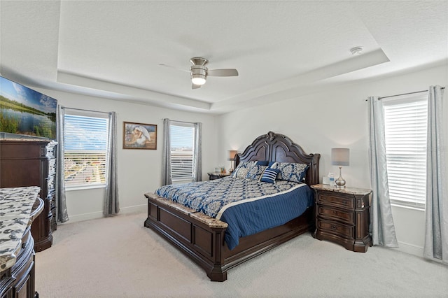 bedroom featuring a ceiling fan, a tray ceiling, light colored carpet, and baseboards